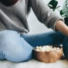 woman sits on a rug with a bowl of popcorn